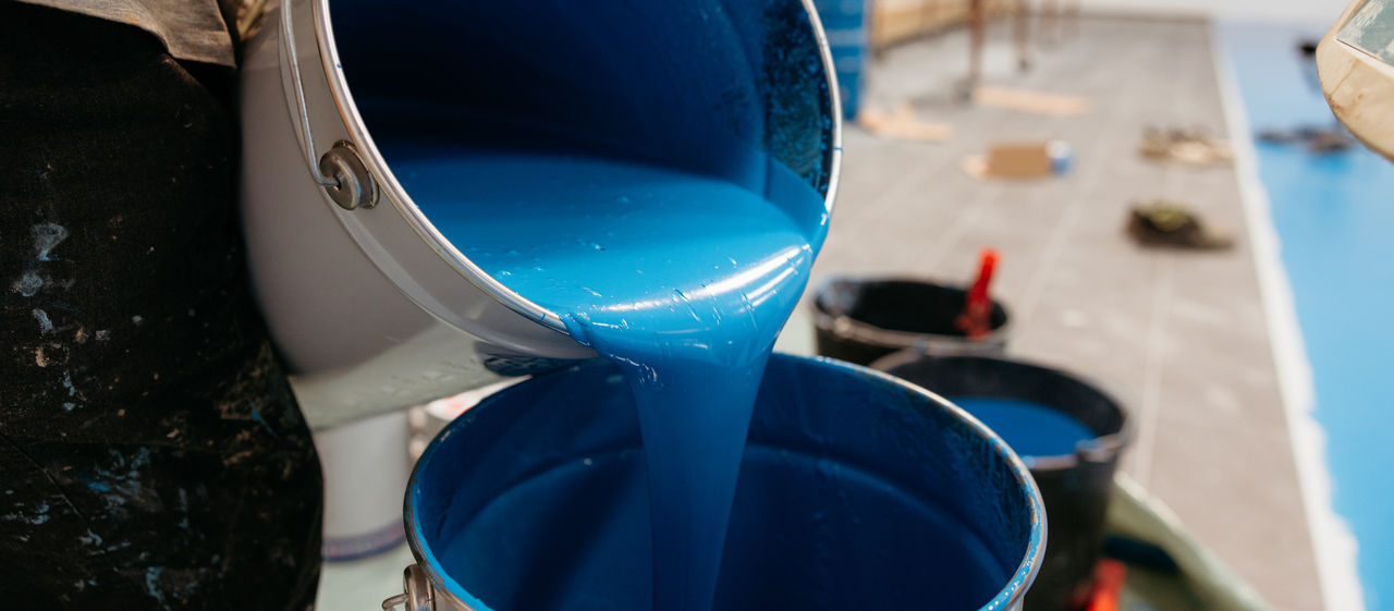 A bucket of blue epoxy being poured into another bucket for coating